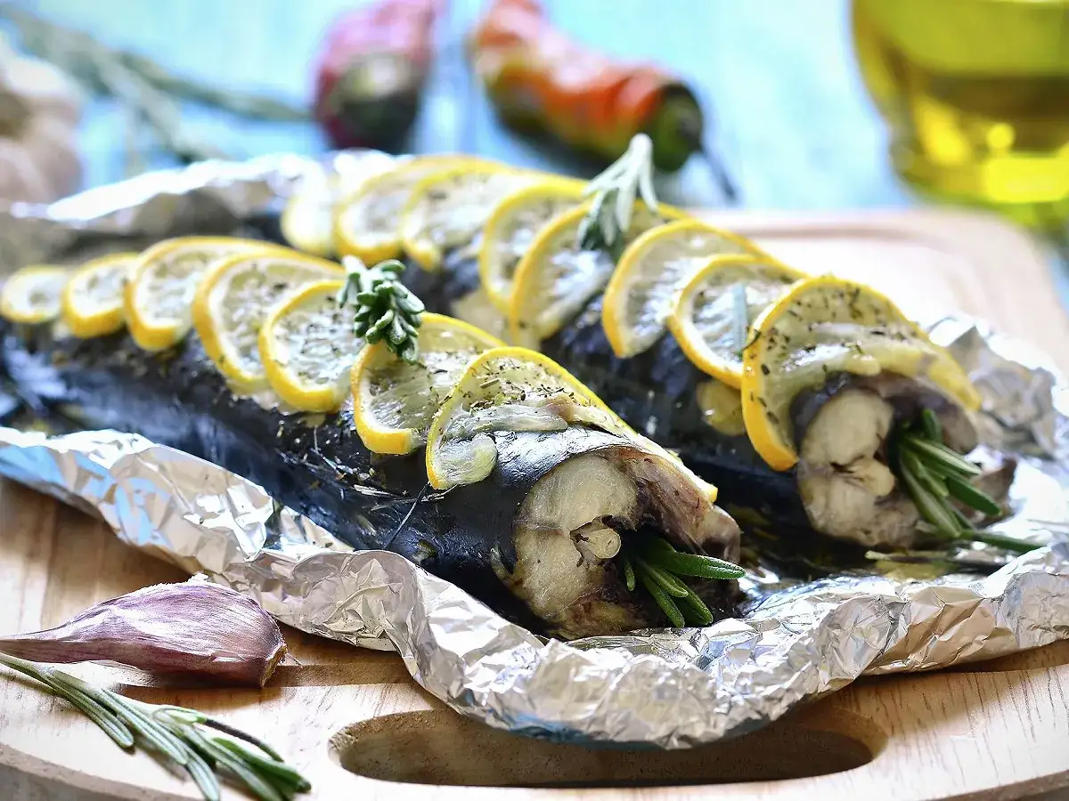 Deux maquereaux en papillote, prêts pour le barbecue, garnis de rondelles de citron et de romarin.