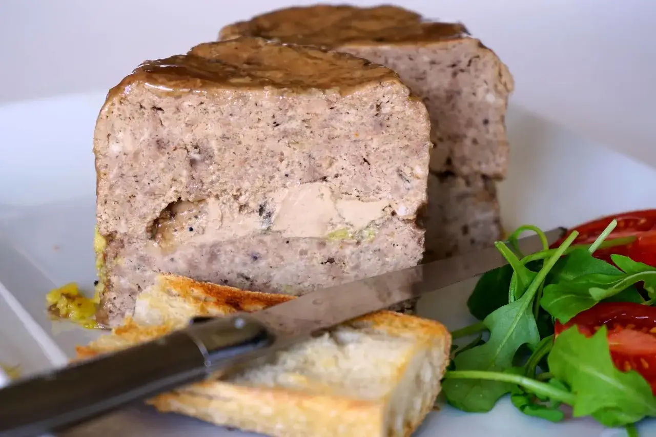 Tranche de terrine de foie de volaille à l'ancienne, garnie de foie gras, servie avec toasts grillés et salade fraîche.