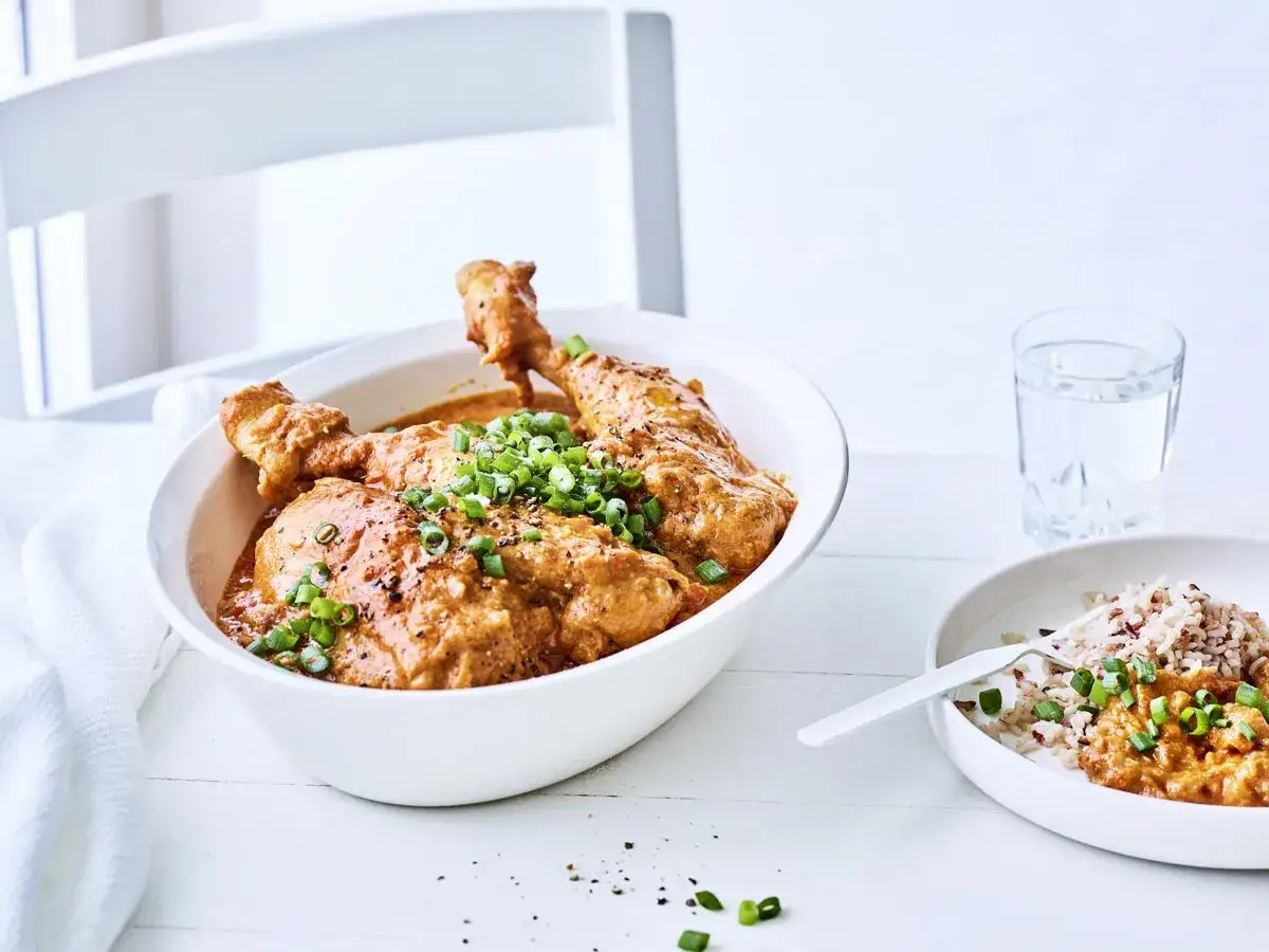 Un plat de poulet moambe crémeux, garni de ciboule fraîche, servi dans un bol blanc avec du riz à côté.