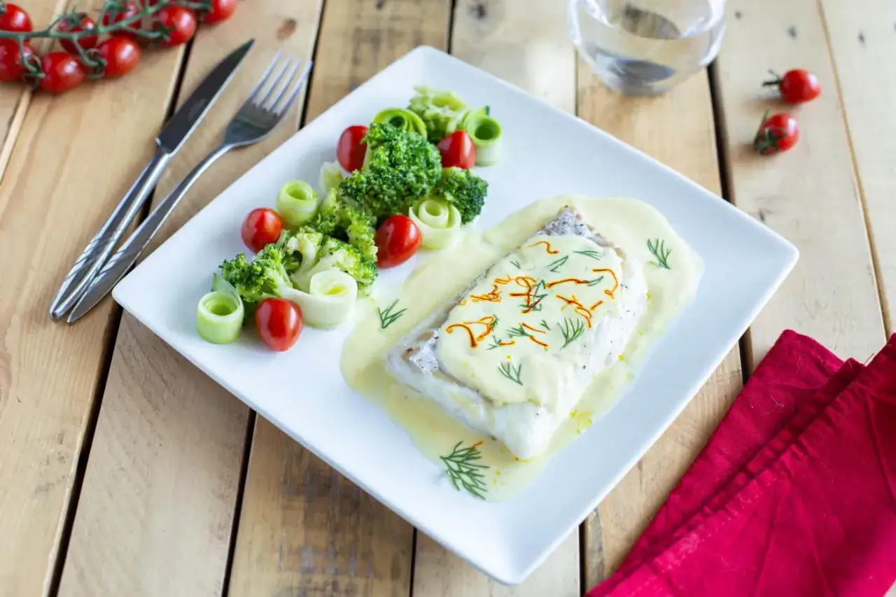 Dos de cabillaud au four, nappé d'une sauce onctueuse au vin blanc et crème fraîche, accompagné de brocolis, tomates cerises et rouleaux de concombre.