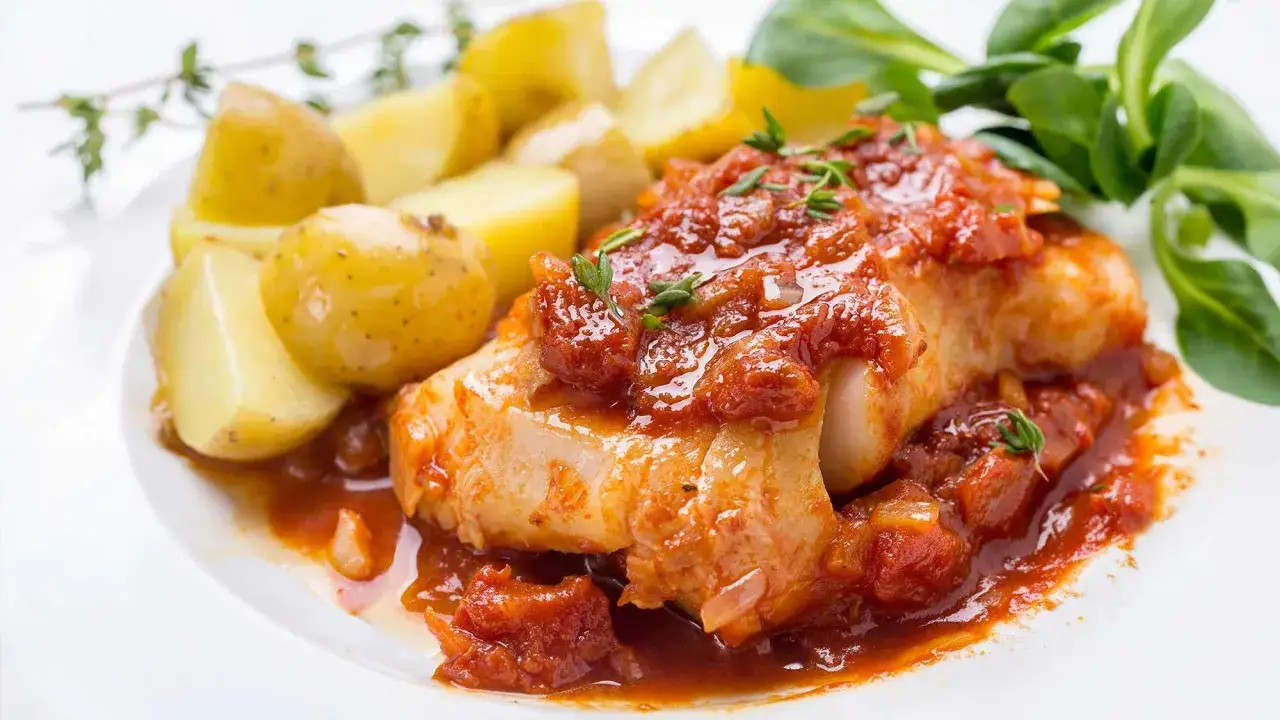 Dos de cabillaud à la provençale au four, nappé d'une sauce tomate savoureuse, servi avec des pommes de terre rôties et une touche de verdure.