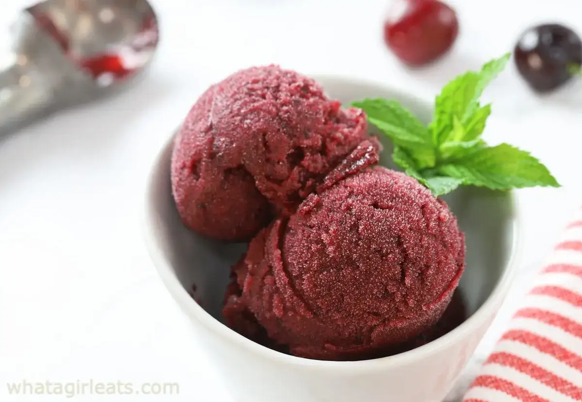 Deux boules de sorbet cerise maison dans un bol blanc, garnies de menthe. Parfait pour une recette sorbet cerise rafraîchissante.