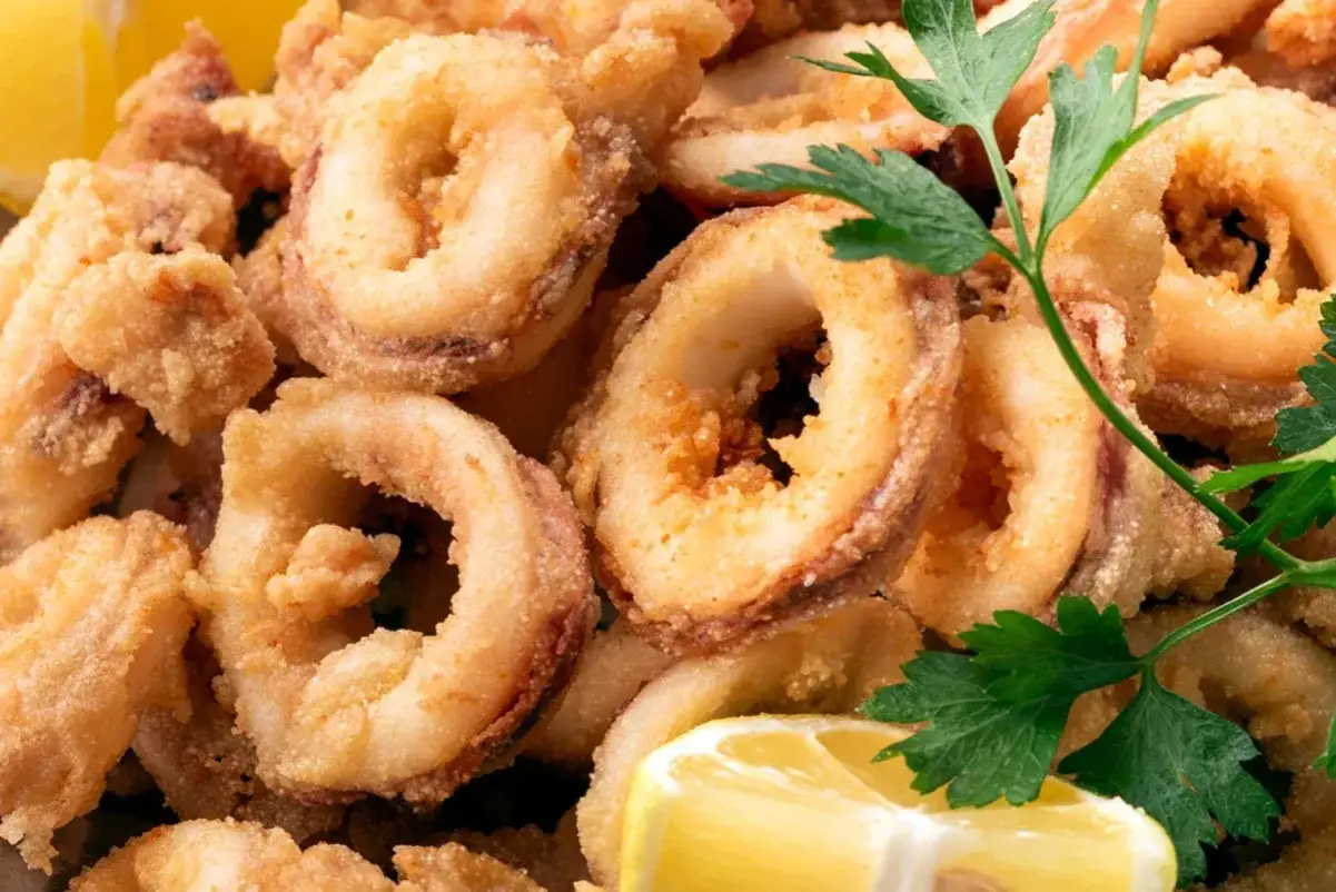 Des anneaux de calamar à l'andalouse, dorés et croustillants, servis avec du persil frais et des quartiers de citron. Un délice !