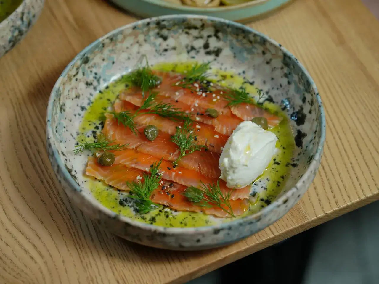 Saumon gravlax maison, fines tranches de poisson cru mariné, garnies d'aneth, de câpres et d'une quenelle de crème fraîche.