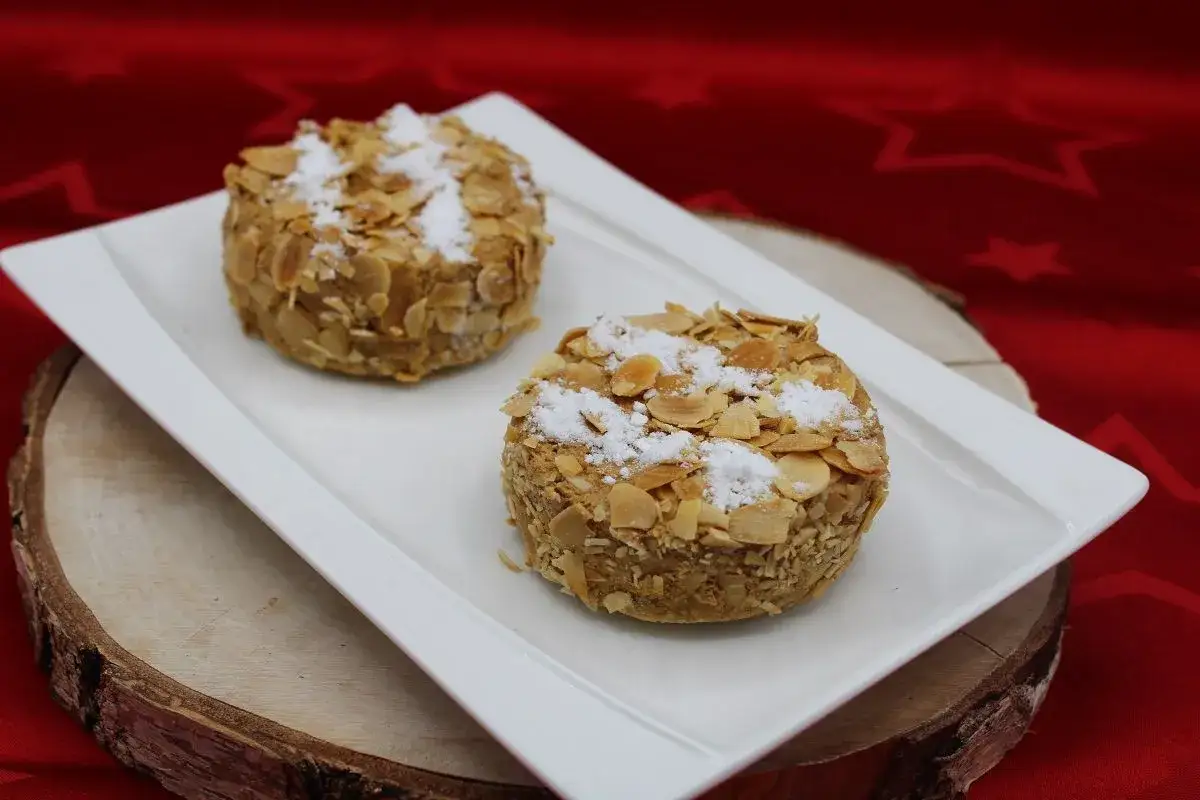 Deux petites charlottes Malakoff, enrobées d'amandes effilées et saupoudrées de sucre glace, sur une assiette blanche.