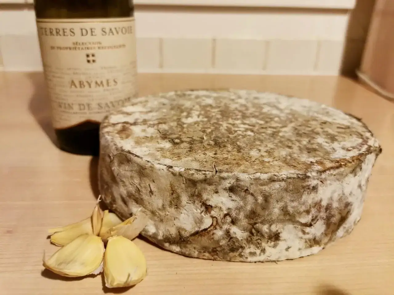 Un fromage matouille d'origine savoyarde, avec une tête d'ail et une bouteille de vin de Savoie.