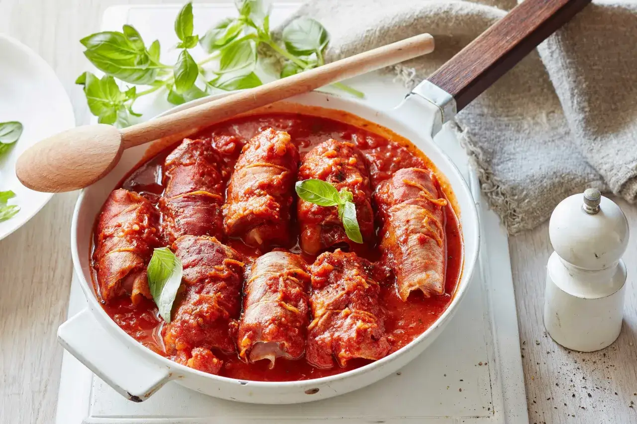 Involtini de boeuf mijotant dans une sauce tomate savoureuse, garni de basilic frais. Un plat réconfortant prêt à être dégusté.