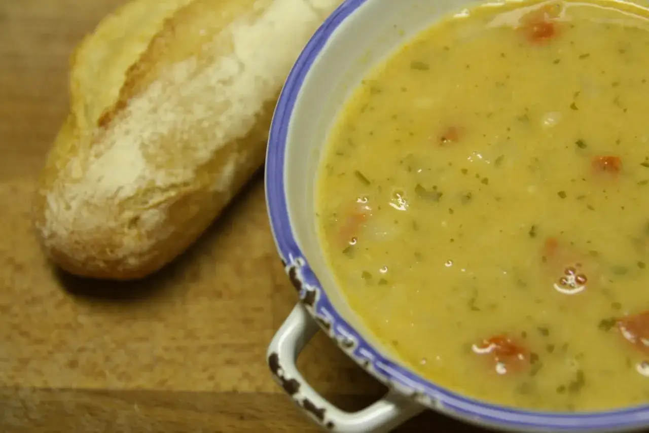 Un bol de soupe haricots blancs crémeuse avec des morceaux de tomates et des herbes, accompagné d'une baguette croustillante sur une planche en bois.