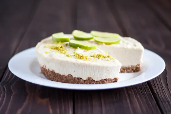 Un délicieux gâteau zéphyr crémeux, garni de fines tranches de citron vert et de zestes, sur une assiette blanche.