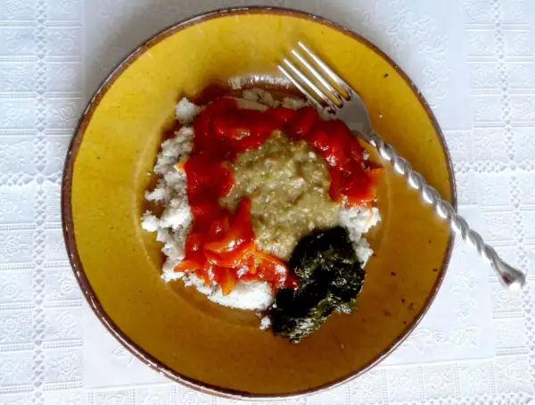 Un plat guinéen facile : riz blanc, sauce verte, sauce tomate et feuilles de manioc sur une assiette jaune.