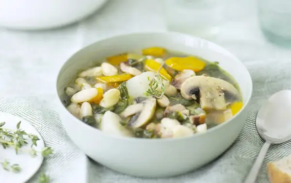 Un bol de soupe haricots blancs réconfortante avec des champignons, des carottes et des herbes fraîches.