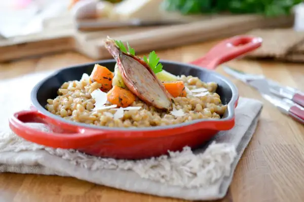 Un savoureux risotto d'épeautre garni de carottes rôties et d'une échalote confite, servi dans une cocotte rouge.