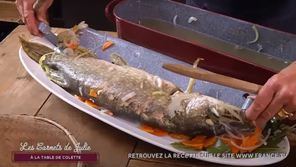 Un brochet au court-bouillon, prêt à être servi avec une mayonnaise maison. Il est garni de carottes et d'oignons.