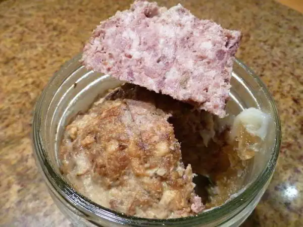 Un bocal de marmiton pâté de sanglier en bocaux stérilisés, avec une tranche de pâté posée sur le bord.