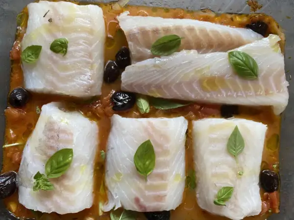 Cinq pavés de dos de cabillaud à la provençale au four, baignant dans une sauce tomate et olives, ornés de feuilles de basilic frais.