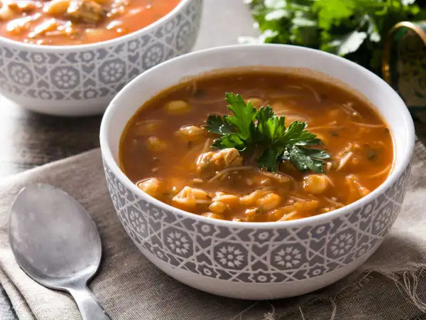 Un bol de recette harira berbère, une soupe réconfortante aux pois chiches, viande et vermicelles, garnie de persil frais.