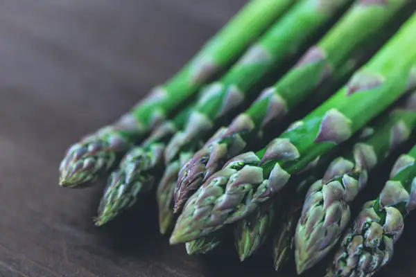 Un bouquet de pousses d'asperges vertes, aux pointes violettes, repose sur une surface en bois sombre.