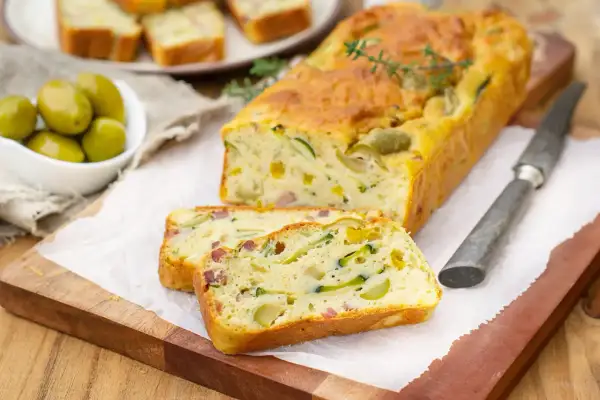Savoureux cake salé aux courgettes et olives, parfait pour une recette d'oreille d'ours. Servi tranché sur une planche en bois.
