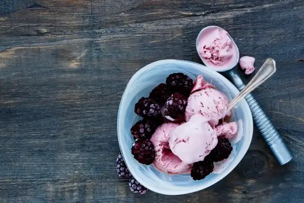 Délicieuse recette de glace avec fruits congelés et yaourt, garnie de mûres fraîches. Une cuillère sert la glace rose crémeuse.