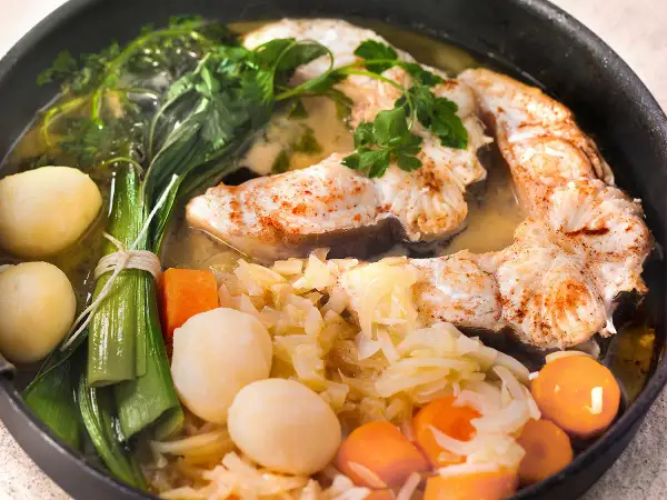 Un plat appétissant de daube de congre, avec des morceaux de poisson tendres, des pommes de terre, des carottes et des poireaux, le tout mijoté dans un bouillon savoureux.