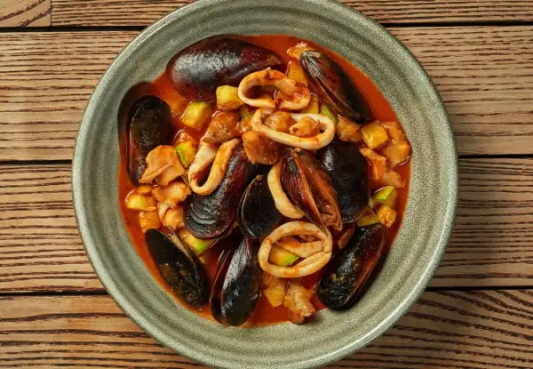 Zarzuela la vraie recette espagnole : un plat de fruits de mer savoureux avec des moules, des calamars et des légumes dans une sauce rouge.