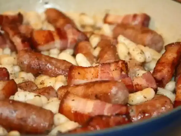 Saucisses catalanes enveloppées de lard, mijotant avec des haricots blancs. Une recette savoureuse à découvrir.