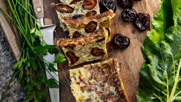 Tranches de **punti salé** aux pruneaux, sur une planche en bois, avec des herbes fraîches et des feuilles vertes.