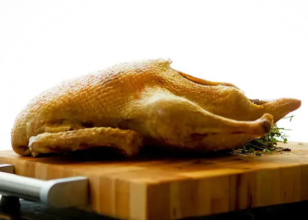 Canard entier doré, prêt pour une recette tanche entière au four. Sur une planche en bois, avec des herbes.