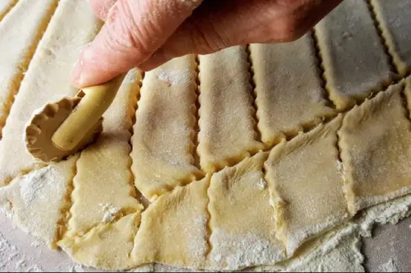 Main d'une personne utilisant une roulette pour découper une pâte à gâteau en losanges.