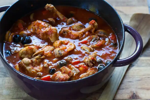 Un plat mijoté de râble de lapin à la provençale, avec des olives noires et des champignons, dans une cocotte en fonte.
