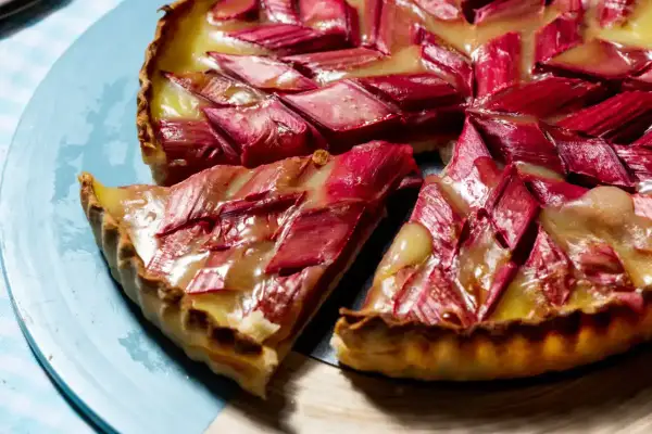 Tarte rhubarbe/pommes crémeuse aux éclats rouges et dorés, une part coupée sur une assiette bleue.
