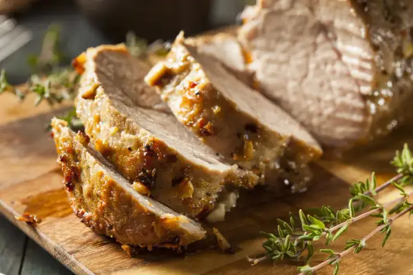 Tranches de porc rôti, parfaites pour le temps de cuisson cochon de lait au barbecue. Garnies d'herbes fraîches sur une planche en bois.