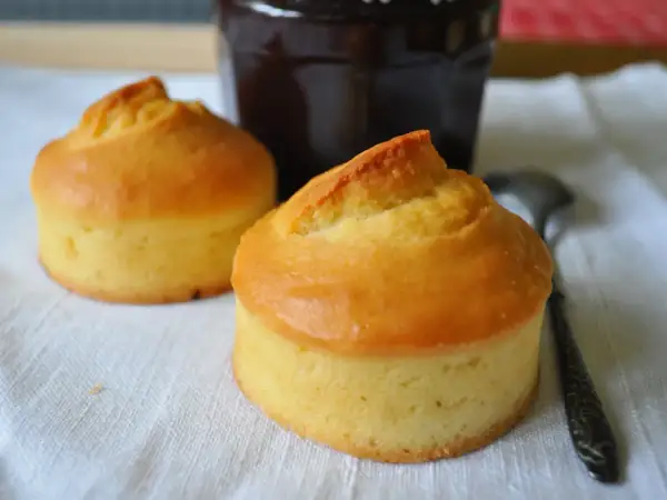 Deux petits gâteaux dorés, rappelant les vieilles recettes de gâteau à la peau de lait, sont prêts à être dégustés avec un pot de confiture sombre.