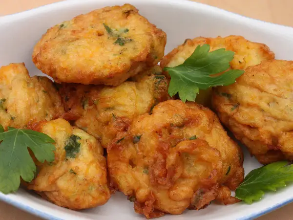 Des beignets dorés et croustillants, comme les farinettes de grand-mère, garnis d'herbes fraîches, dans un plat blanc.